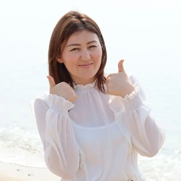 Smiling dark haired girl on seashore with thumbs up. How to Best Your IELTS Writing Test: 48 Awesome Tips