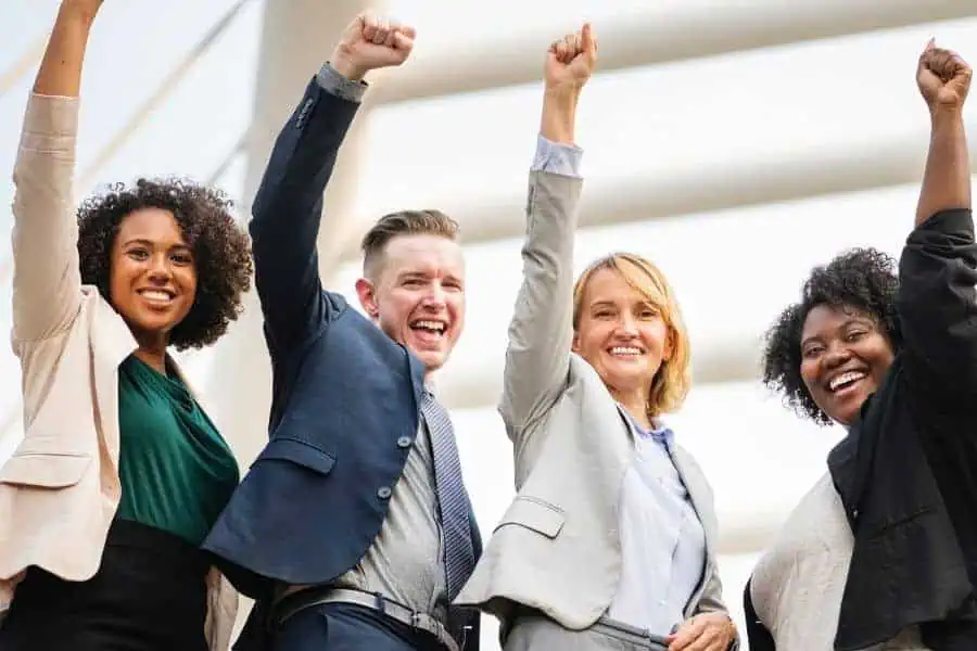 A few young, well dressed people smiling with their hands in the air