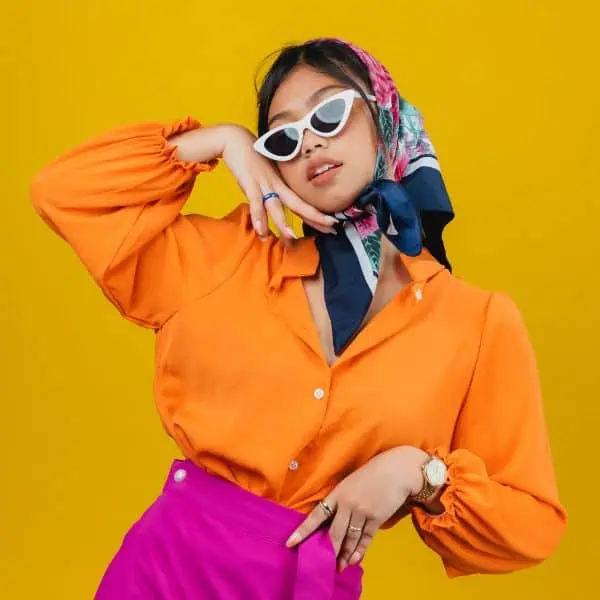 Dark haired young woman wearing sunglasses, a headscarf, an orange shirt and pink skirt against a yellow background - Latest IELTS Speaking Questions September to December 2024